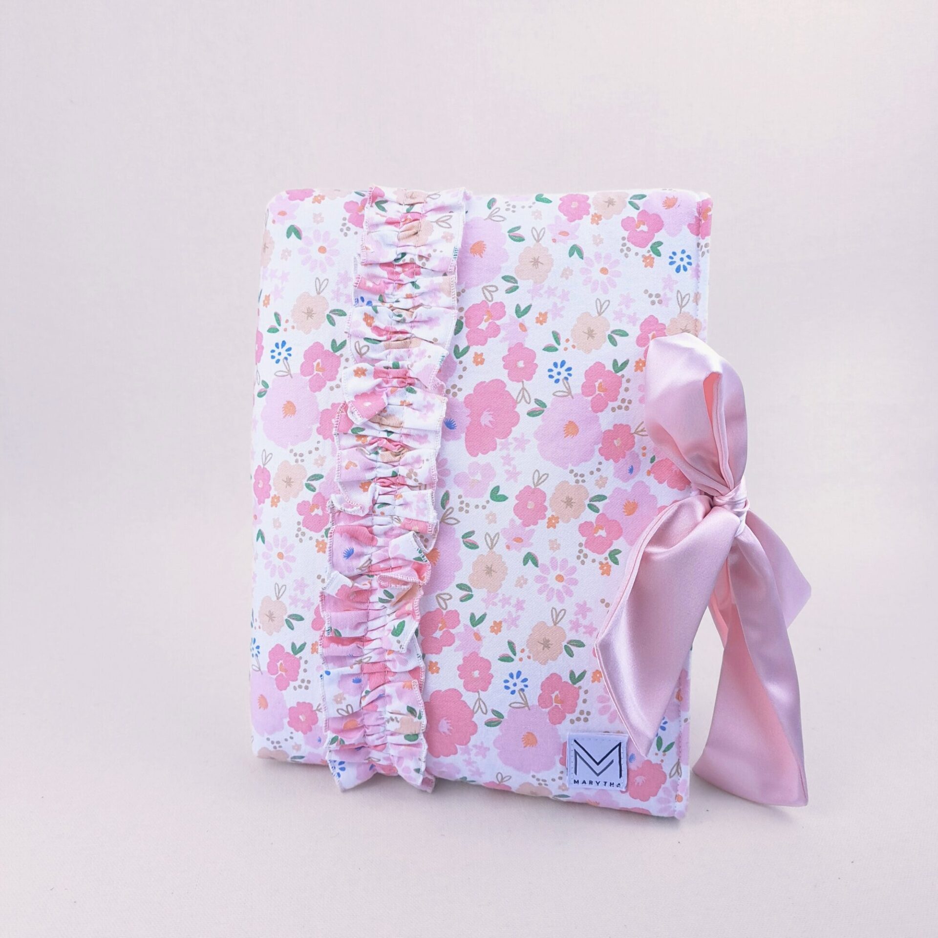 A delicate pink floral bow Bible sleeves featuring a ruffled design and a satin bow closure. This Bible sleeve is perfect for women seeking a stylish and feminine way to protect their Bibles or journals.